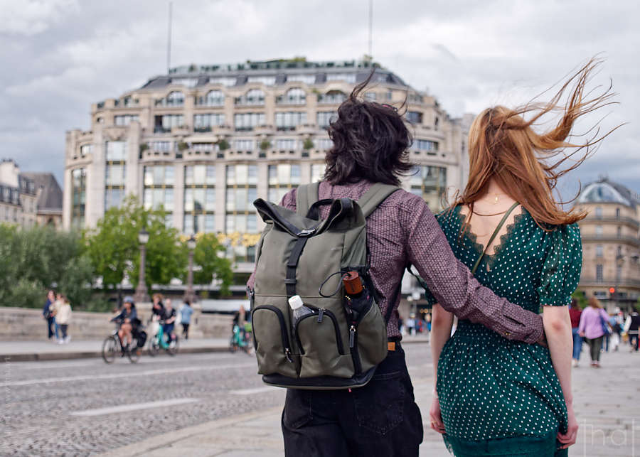 A couple seen from behind, their hair blowing in the wind, on the Pont Neuf in Paris