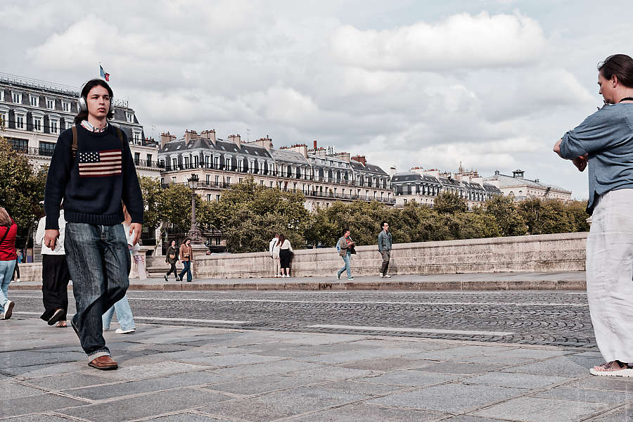 A man walking across the Pont Neuf wearing a sweater with an American flag pattern