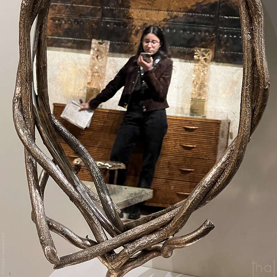 reflet d'une femme tenant sont téléphone dans un miroir au cadre en forme de branchages