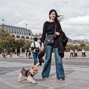 A young woman walking a small dog on a leash on the Pont Neuf in Paris