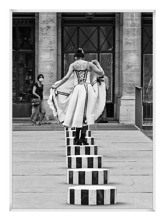 Tirage d'art en noir et blanc d'une danseuse vue de dos soulevant sa jupe dans la cours du Palais Royal à Paris