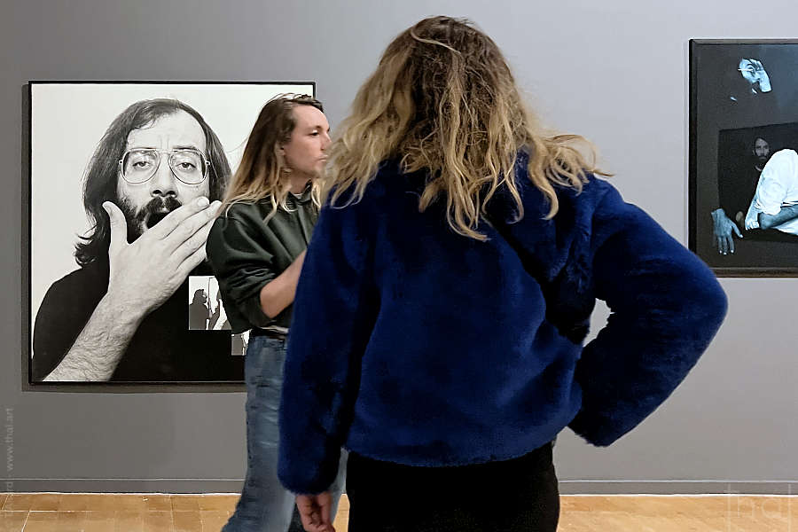 un couple sans interaction devant une photographie de visage d'homme nez-à-nez avec la sculpture du visage de Guillaumon en train de bailler