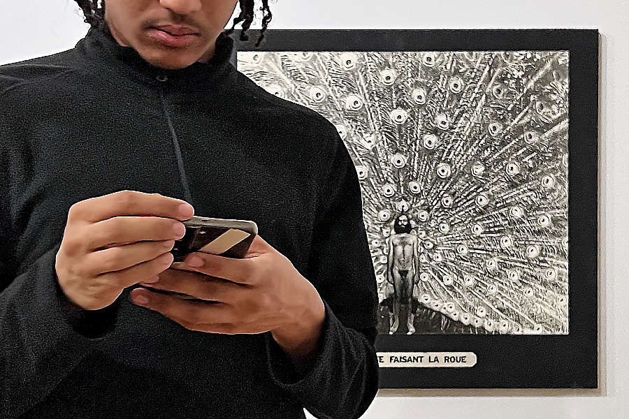Jeune homme tenant un smartphone et tournant le dos à une photographie de Jean-Claude Guillaumon