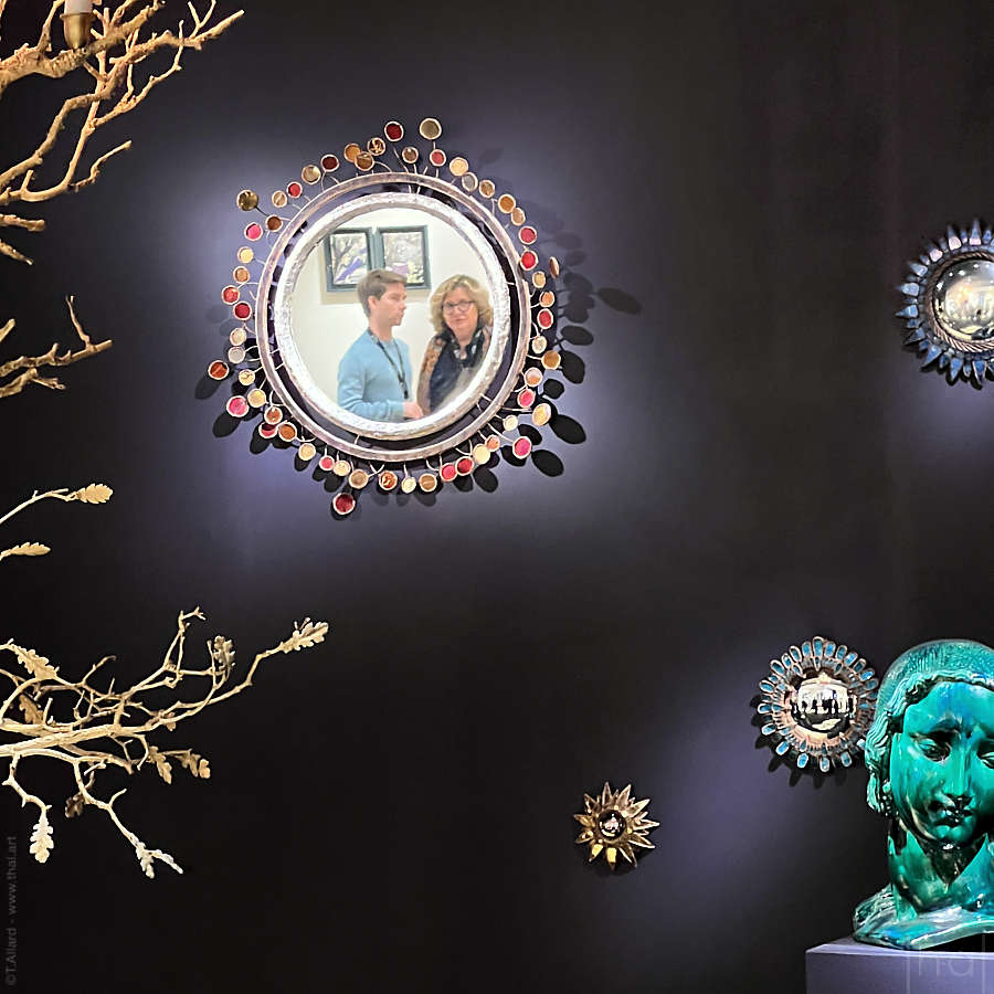 mur aubergine avec des petits miroirs dont l'un reflète deux visiteurs