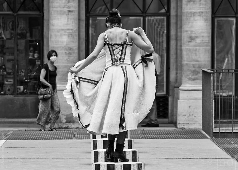 Danseuse en noir et blanc vue de dos et soulevant sa jupe devant une passante dans la cours du Palais Royal
