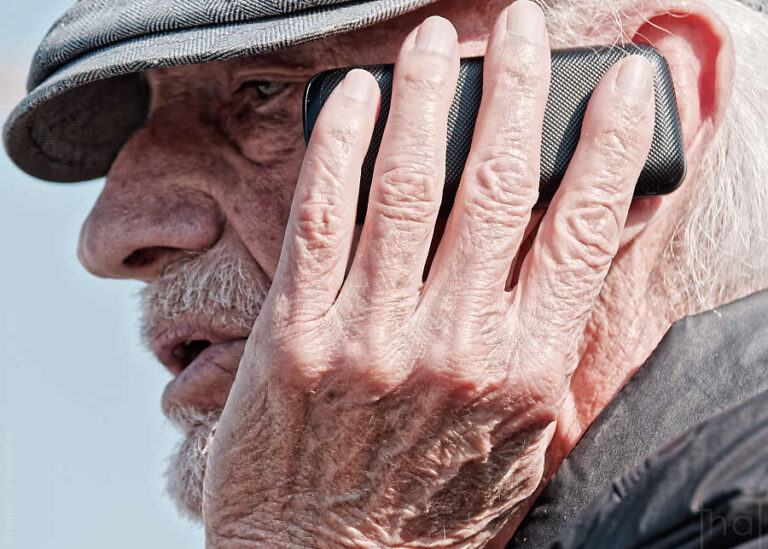 main ridée plaquant un téléphone sur le visage d'un viel homme